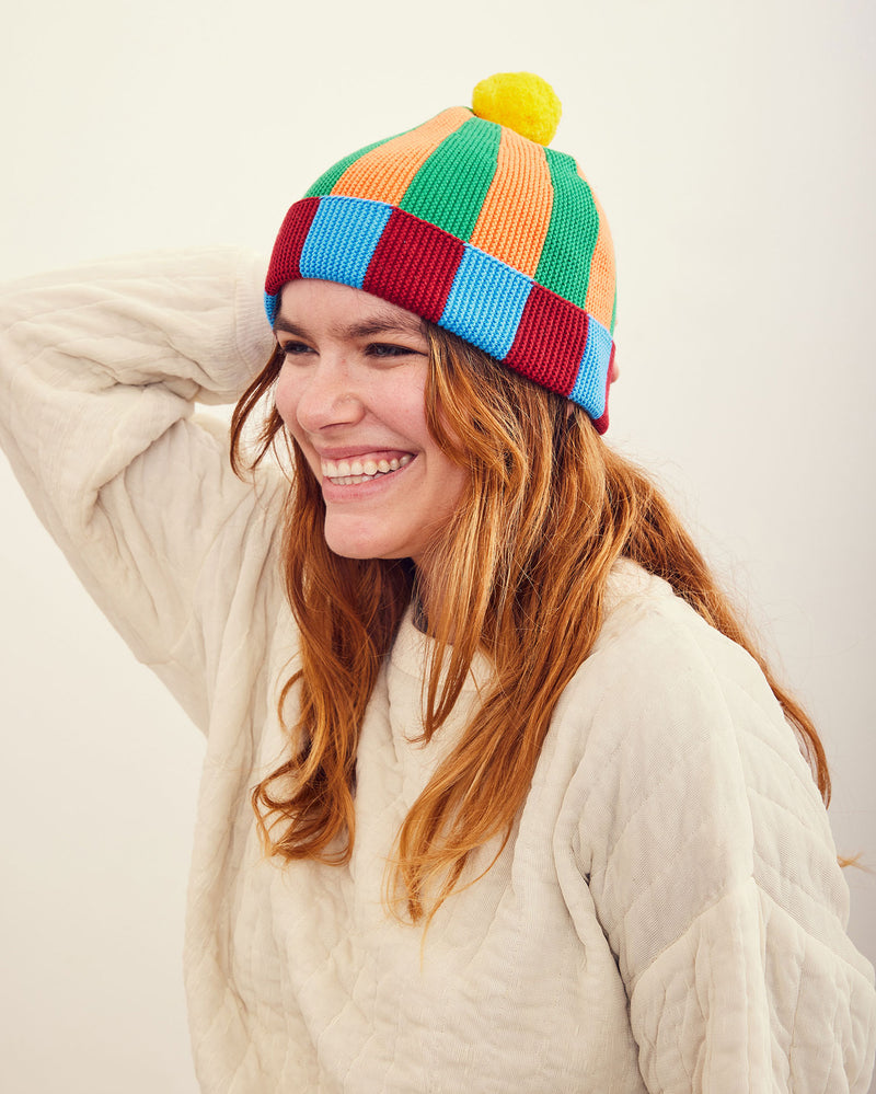 Zucchini Stripe Hat. Ribbed-knit pom beanie with contrasting orange, green, rhubarb, and marina blue stripes. 100% Cotton. Made in China.