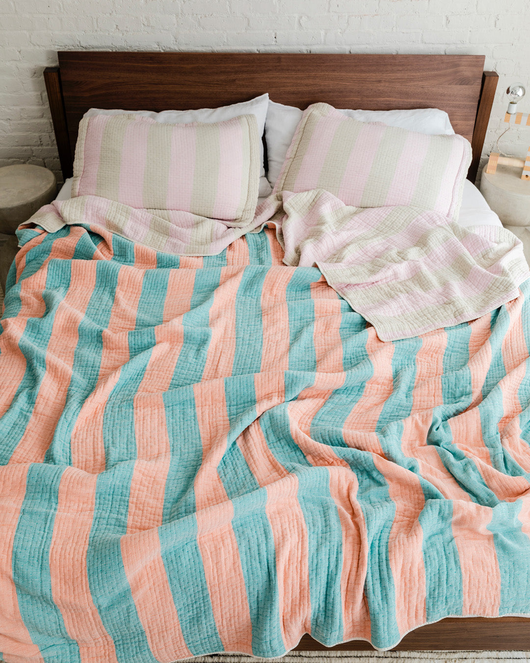 Dusen Dusen Warm Stripe Coverlet Set in reversible stripe colorways. Pink and beige stripes on one side, orange and green stripes on the other side. Woven matelassé coverlet with an inner layer of insulation for a quilted effect. Stonewashed, with an extra soft and gauzy hand feel. 100% cotton shell, polyester fill. Machine wash cold and tumble dry low. Made in Portugal.